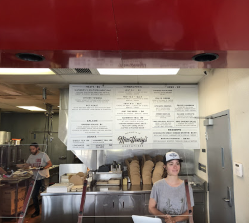 A woman stands at a counter in a restaurant, with a menu displayed on the wall behind her.
