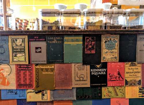 A colorful display of vintage books on a shelf, with jars and a café setting in the background.