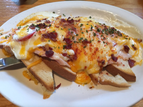 A plate of toast topped with melted cheese, bacon, and herbs, served with a side of creamy sauce.