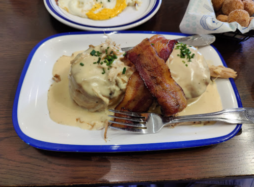 A plate of biscuits topped with creamy sauce and crispy bacon, garnished with chives.