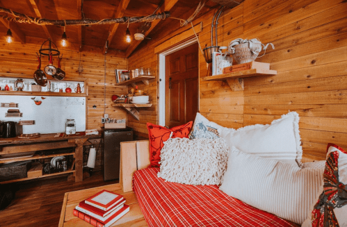 Cozy wooden cabin interior with a red and white sofa, shelves, and warm lighting, creating a rustic atmosphere.