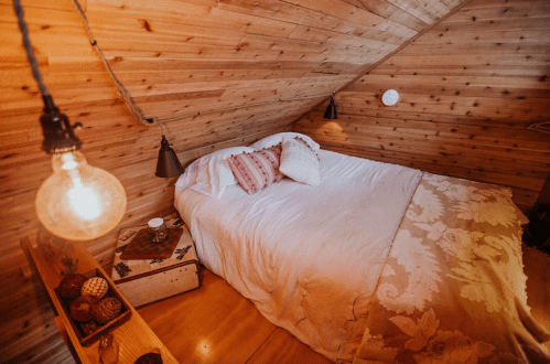 Cozy attic bedroom with a sloped wooden ceiling, a bed with pillows, and warm lighting.