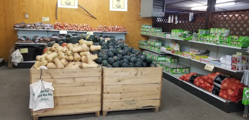 A produce market with wooden crates of squash and pumpkins, and shelves stocked with various packaged goods.