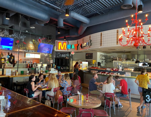 A lively restaurant interior with colorful decor, featuring diners at tables and a vibrant "Meat Free" sign.
