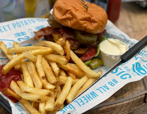 A delicious burger with toppings on a tray, accompanied by a side of crispy fries and dipping sauce.