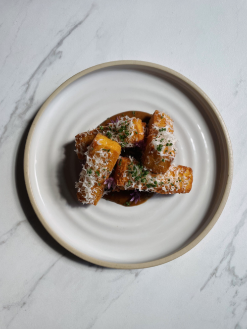 A plate of golden fried food topped with grated cheese and herbs, set against a marble background.