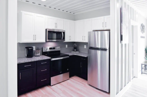 Modern kitchen with white and black cabinets, stainless steel appliances, and light wood flooring.