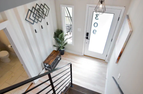 A modern entryway with a staircase, decorative wall art, a plant, and a glass door displaying the number 30.