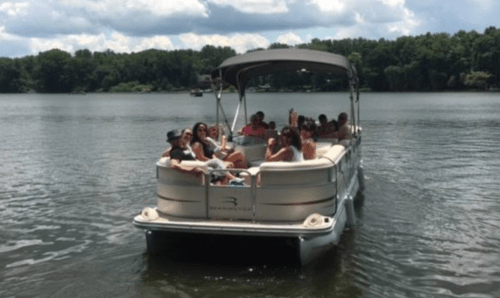 A group of people enjoying a sunny day on a pontoon boat on a lake surrounded by trees.