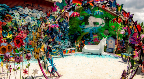 Colorful outdoor art installation featuring flowers, a unicorn statue, and vibrant murals in a whimsical setting.