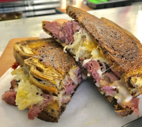 A close-up of a grilled sandwich with layers of meat, cheese, and sauerkraut on toasted rye bread.