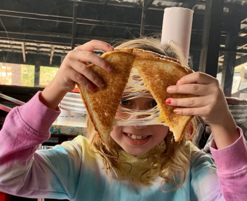 A child holds a grilled cheese sandwich, showcasing the gooey cheese stretching between the two slices.