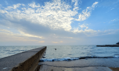A serene view of a calm lake under a cloudy sky, with a concrete pier extending into the water.