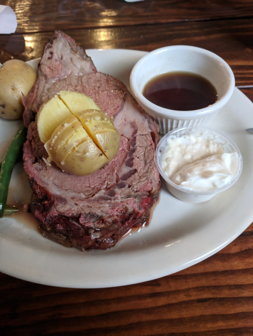 A plate with sliced roast beef, a baked potato, green beans, and dipping sauces.