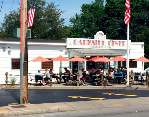 A diner with outdoor seating under orange umbrellas, surrounded by trees and American flags.