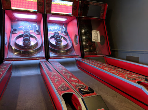 Three red and black skee-ball machines lined up against a wall, with illuminated scoring displays.