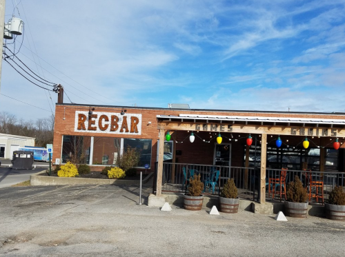 Exterior of REC BAR, a brick building with colorful lights, surrounded by planters and a parking area.