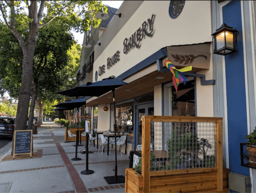 A charming bakery with outdoor seating, colorful flags, and a welcoming entrance on a sunny street.