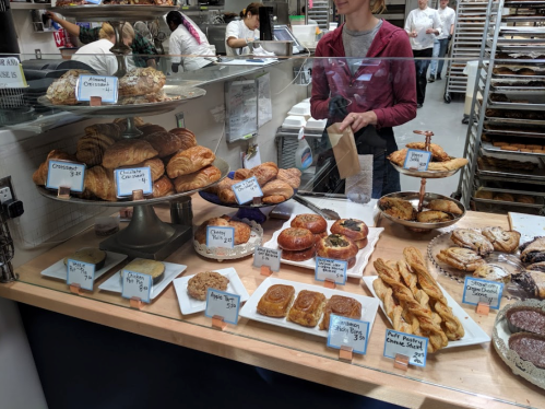 A bakery display case filled with various pastries, including croissants, danishes, and cookies, with prices labeled.