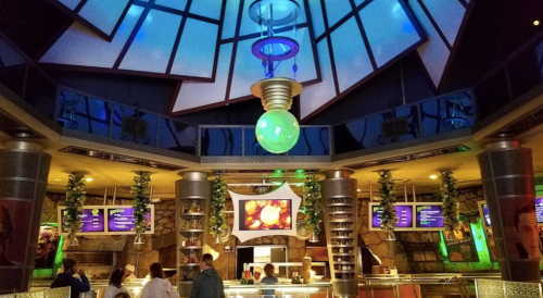 A modern restaurant interior with colorful lighting, a large green pendant light, and a menu display.