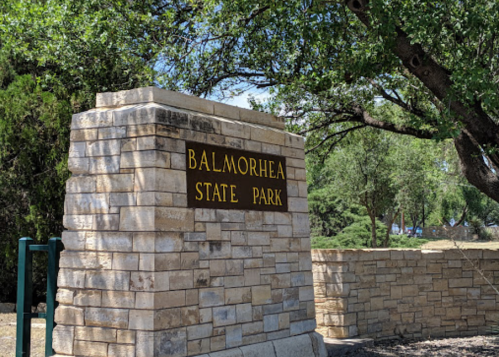 Sign for Balmorhea State Park, featuring stone structure and greenery in the background.