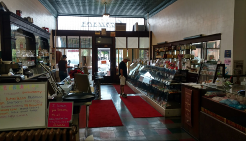 A vintage shop interior with display cases, a red carpet, and customers browsing various items.