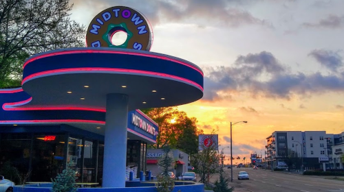A retro diner sign at sunset, with colorful neon lights and a street view of nearby buildings.