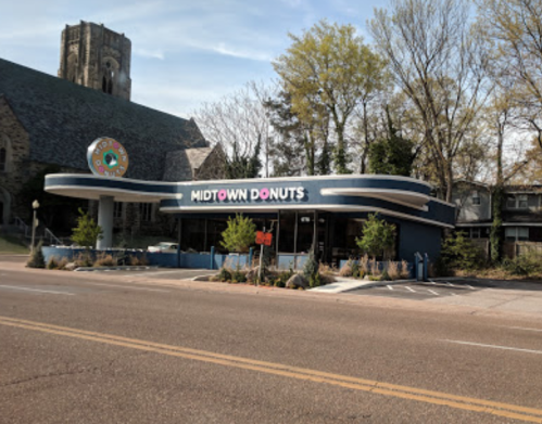A retro-style donut shop named "Midtown Donuts" with a blue exterior and a colorful sign, set on a tree-lined street.