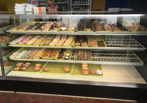 A display case filled with various colorful donuts and pastries, with a person in the background.