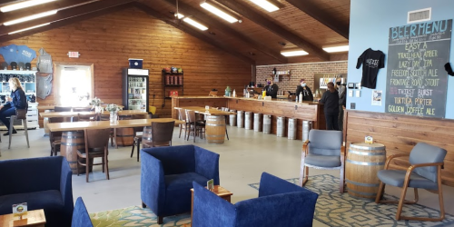 Interior of a brewery with wooden decor, tables, and a bar. People are serving drinks and enjoying the space.