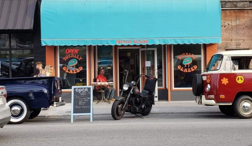 A colorful storefront with a blue awning, a motorcycle parked out front, and a vintage van nearby. Outdoor seating visible.