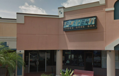 Exterior of Player 1 Video Game Bar, featuring a colorful sign and palm trees in front.