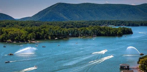 A scenic view of a lake surrounded by mountains, with boats and water sprays creating a lively atmosphere.