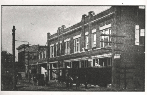 Historic brick buildings with storefronts, featuring early 20th-century architecture and people in front.