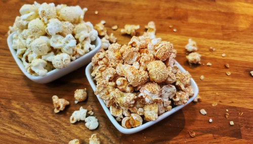 Two bowls of popcorn on a wooden surface: one with plain popcorn and the other with cheese-flavored popcorn.