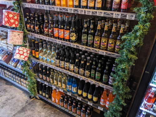 A display of various soda bottles on shelves, decorated with green garland and holiday-themed items.