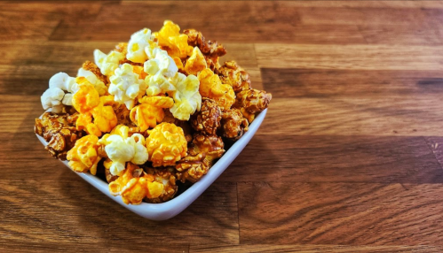 A bowl of colorful popcorn, including yellow, orange, and white varieties, on a wooden surface.