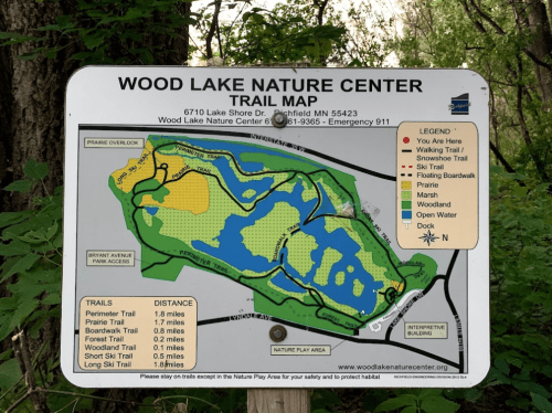 Trail map of Wood Lake Nature Center, showing paths, water areas, and surrounding nature features. Emergency contact info included.