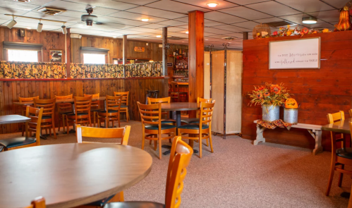 Cozy restaurant interior with wooden decor, empty tables, and autumn-themed decorations on a side table.