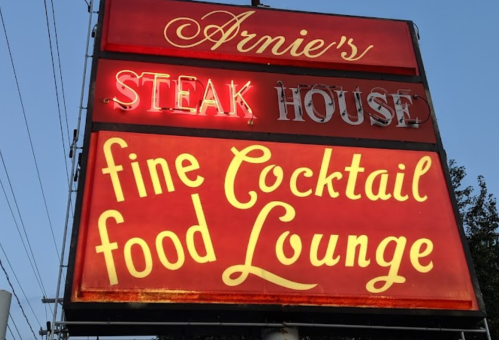 Sign for Arnie's Steak House featuring "fine Cocktail food Lounge" in bright red and yellow lettering.