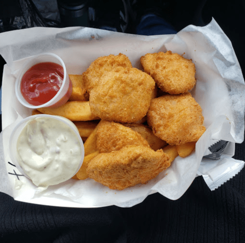 A tray of golden fried chicken nuggets and fries, served with ketchup and a creamy dipping sauce.