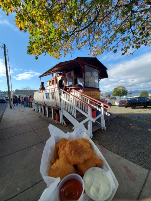 A food stand with a line of customers, featuring a plate of fried food and dipping sauces in the foreground.
