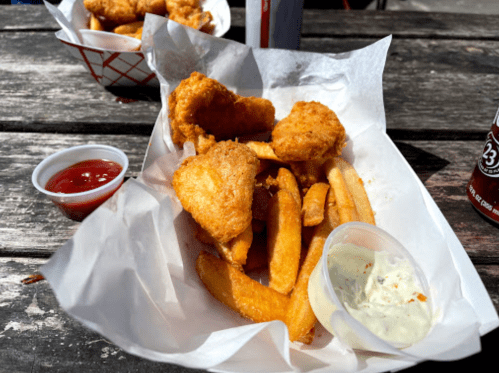 A plate of golden fried fish and crispy fries, served with ketchup and a creamy dipping sauce on a wooden table.