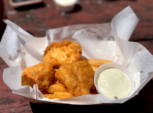 A basket of golden fried fish pieces and crispy fries, served with a small cup of dipping sauce.