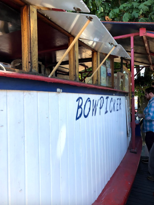A food truck named "Bowpicker" with a wooden exterior, set in a vibrant outdoor location.