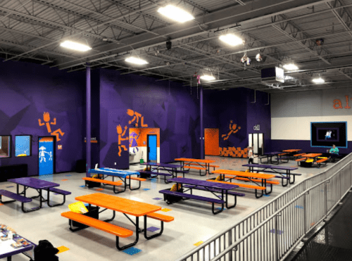 Brightly colored indoor space with orange and purple walls, featuring tables and playful wall art.