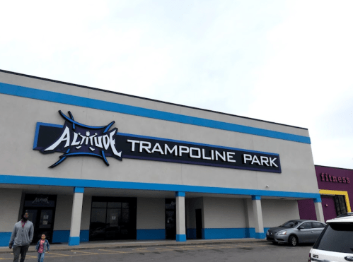 Exterior of Altitude Trampoline Park building with a blue and white facade, featuring a sign and nearby parking lot.