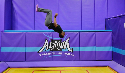 A person performs a backflip on a trampoline at Altitude Trampoline Park, surrounded by purple walls.