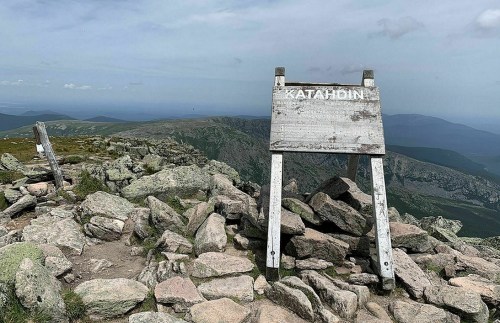Sign marking the summit of Katahdin, surrounded by rocky terrain and distant mountains under a cloudy sky.