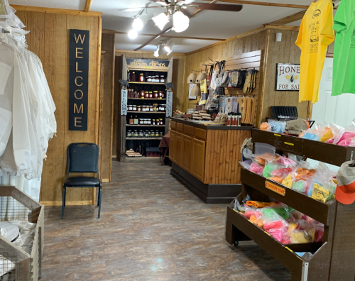 Interior of a rustic shop with wooden walls, a welcome sign, shelves of products, and colorful merchandise displays.
